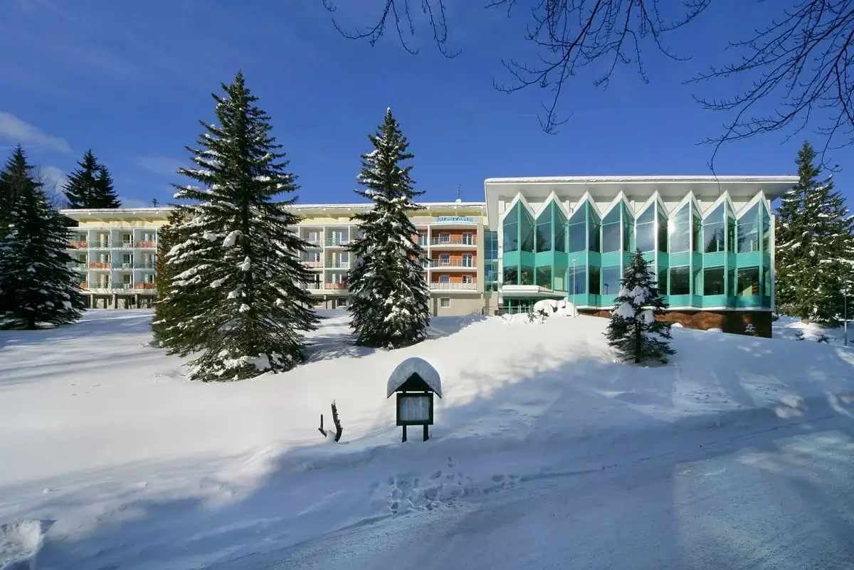 Beskrivelse af Hotellet: Interhotel Montana er et elegant og komfortabelt hotel, der tilbyder en fremragende base for at udforske den naturskønne Spindleruv Mlýn. Hotellet er kendt for sin moderne indretning, høje standard af service og en afslappende atmosfære, der gør det til et ideelt valg for bade ferie- og forretningsrejsende. Med en placering i hjertet af Krkonos-bjergene, giver hotellet nem adgang til en række udendørs aktiviteter hele året rundt. Beliggenhed: Hotellet ligger centralt i Spindleruv Mlýn, en populær destination i Tjekkiets Krkonos-bjerge. Denne centrale placering gør det nemt for gæsterne at nå skiområderne om vinteren og de mange vandre- og cykelruter om sommeren. Faciliteter på Hotellet: Interhotel Montana tilbyder en bred vifte af faciliteter for at sikre et behageligt ophold. Hotellet har en moderne restaurant, bar og loungeområde. Hotellets wellnessområde omfatter sauna og jacuzzi, samt massagebehandlinger. Der er også et fitnesscenter. Værelsesfaciliteter: Værelserne er stilfuldt indrettet med gratis Wi-Fi, fladskærms-tv, minibar, te- og kaffefaciliteter samt eget badeværelse med bruser eller badekar. Mange værelser tilbyder balkon med udsigt over de omkringliggende bjerge eller dalen.